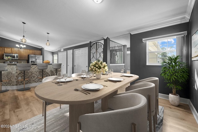 dining space with a notable chandelier, light wood-type flooring, lofted ceiling, and ornamental molding