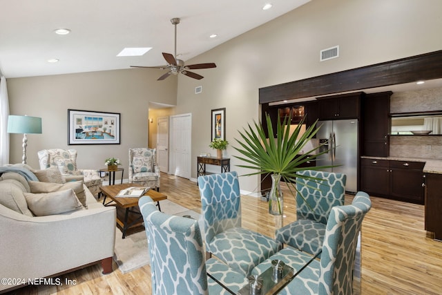 living room featuring a skylight, high vaulted ceiling, ceiling fan, and light hardwood / wood-style floors