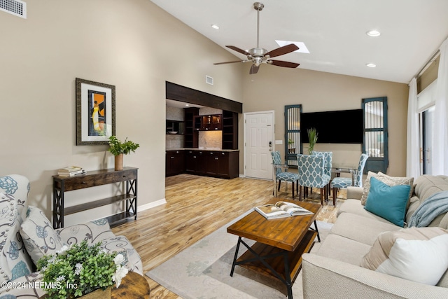 living room featuring a skylight, high vaulted ceiling, ceiling fan, and light hardwood / wood-style flooring