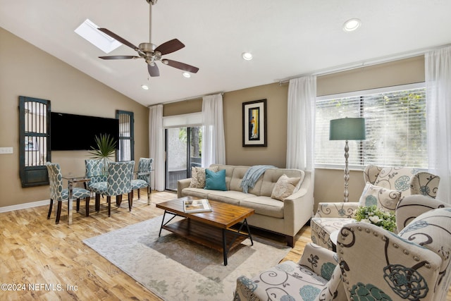 living room featuring lofted ceiling with skylight, ceiling fan, and light hardwood / wood-style flooring