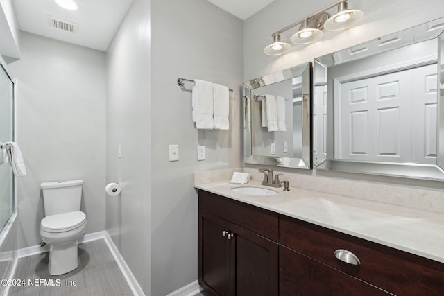 full bathroom with tile patterned floors, vanity, bath / shower combo with glass door, and toilet