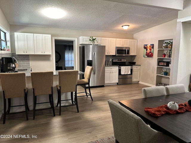 kitchen with a textured ceiling, hardwood / wood-style flooring, white cabinetry, backsplash, and appliances with stainless steel finishes