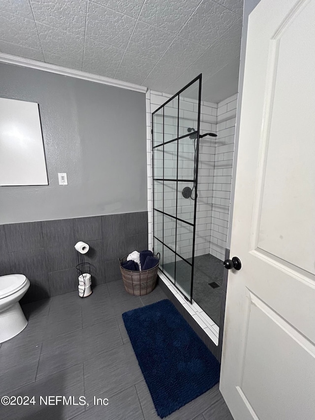 bathroom with a textured ceiling, tiled shower, ornamental molding, and toilet