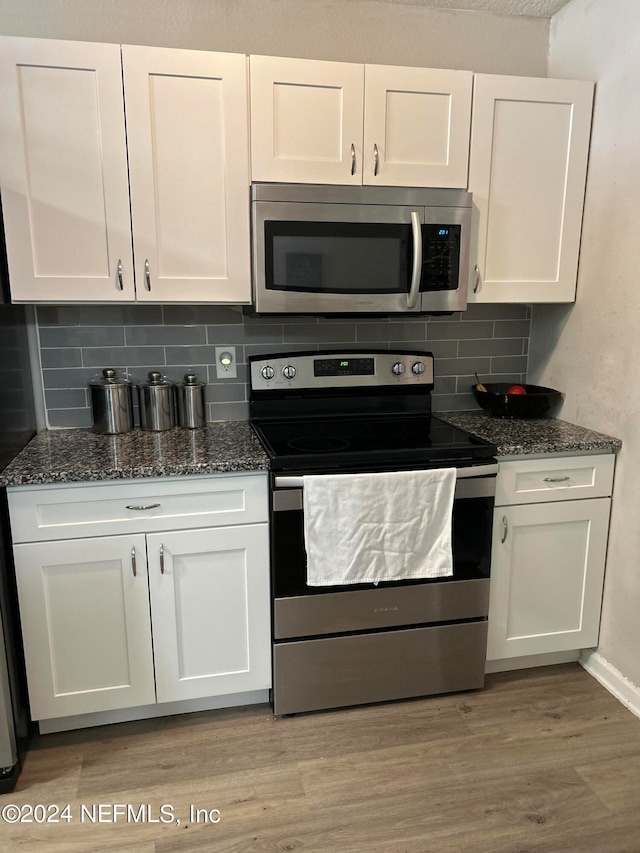 kitchen with dark stone countertops, white cabinetry, tasteful backsplash, stainless steel appliances, and light wood-type flooring