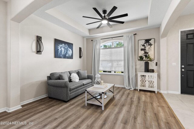 living room featuring wood-type flooring, ceiling fan, and a raised ceiling