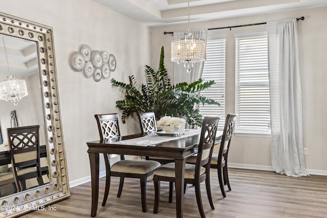 dining area with wood-type flooring, an inviting chandelier, and a raised ceiling