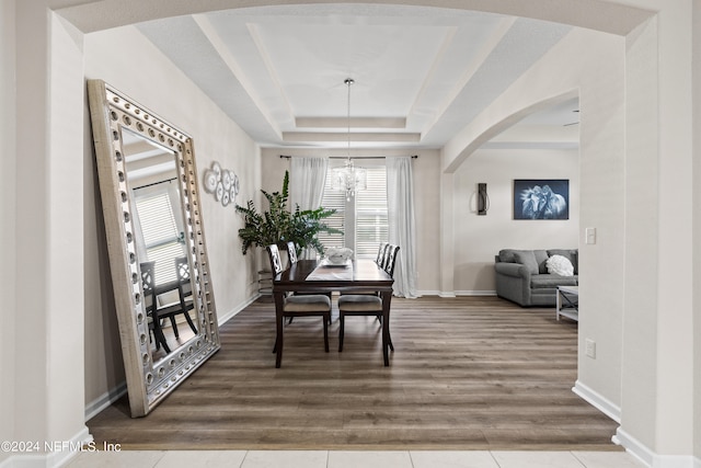 dining room with a notable chandelier, a raised ceiling, and hardwood / wood-style floors