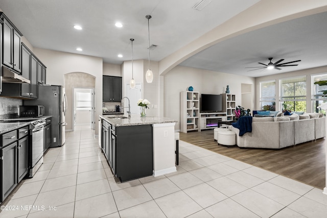 kitchen with ceiling fan, pendant lighting, an island with sink, stainless steel appliances, and light wood-type flooring