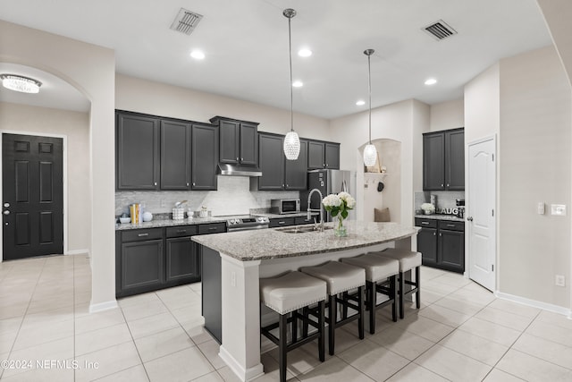 kitchen featuring pendant lighting, light stone counters, a kitchen island with sink, sink, and backsplash