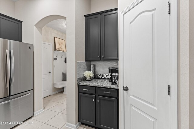 kitchen featuring light stone counters, stainless steel fridge, light tile patterned floors, and tasteful backsplash