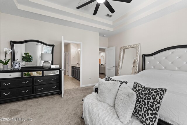 carpeted bedroom with ceiling fan, a raised ceiling, and connected bathroom