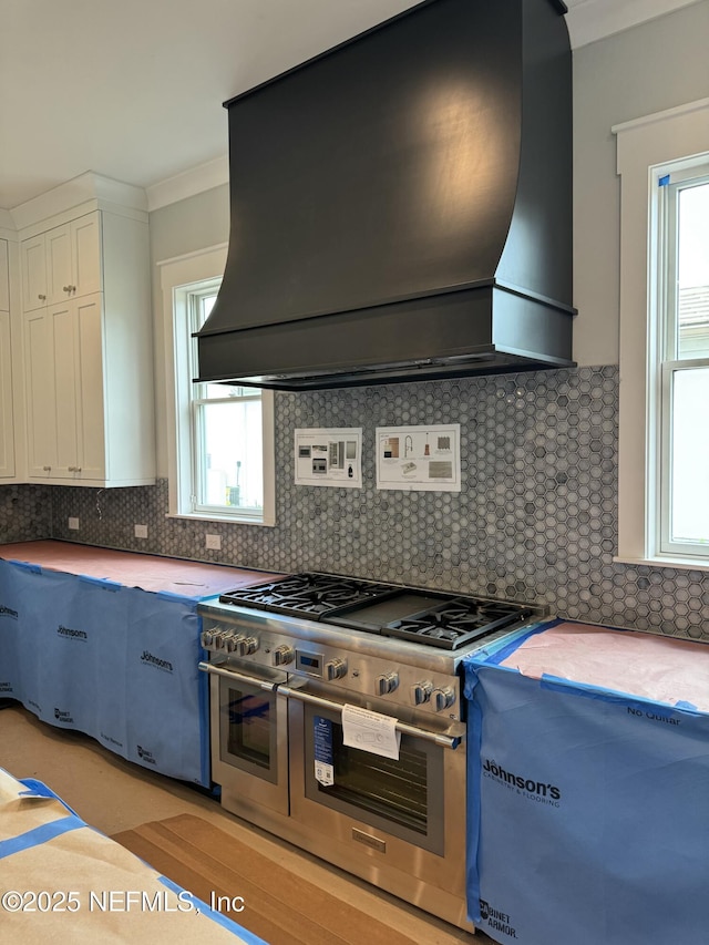 kitchen featuring tasteful backsplash, white cabinetry, ornamental molding, double oven range, and custom range hood