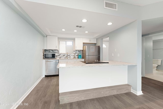 kitchen featuring wood-type flooring, light stone counters, white cabinets, backsplash, and appliances with stainless steel finishes