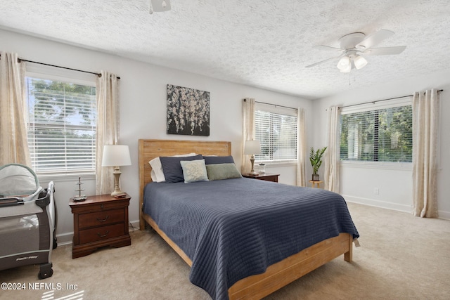 bedroom with ceiling fan, light colored carpet, multiple windows, and a textured ceiling