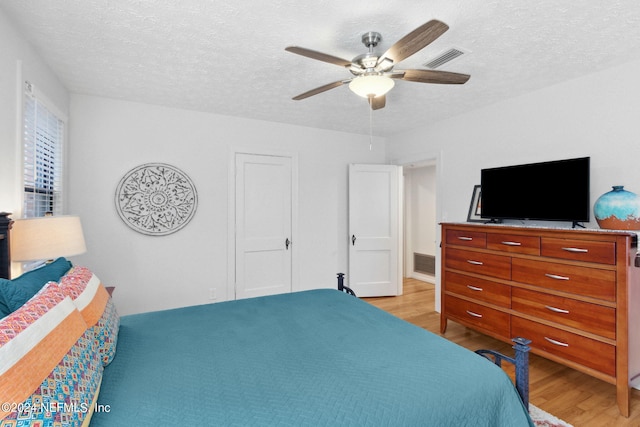 bedroom with light wood-type flooring, a textured ceiling, and ceiling fan