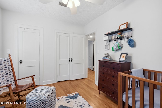 bedroom with a crib, a textured ceiling, light wood-type flooring, and ceiling fan