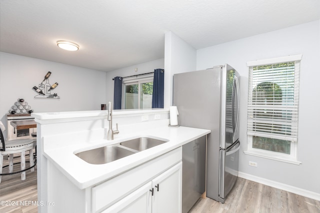 kitchen with white cabinets, sink, light hardwood / wood-style flooring, and a wealth of natural light