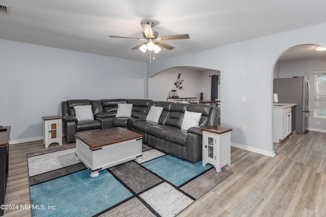 living room with light hardwood / wood-style floors, ceiling fan, and a textured ceiling