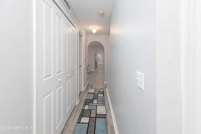 hall featuring a textured ceiling and light hardwood / wood-style flooring