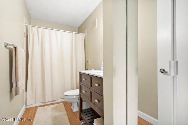 bathroom featuring vanity, curtained shower, a textured ceiling, hardwood / wood-style flooring, and toilet