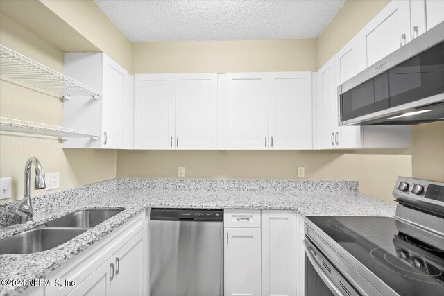 kitchen with appliances with stainless steel finishes, white cabinetry, light stone counters, a textured ceiling, and sink