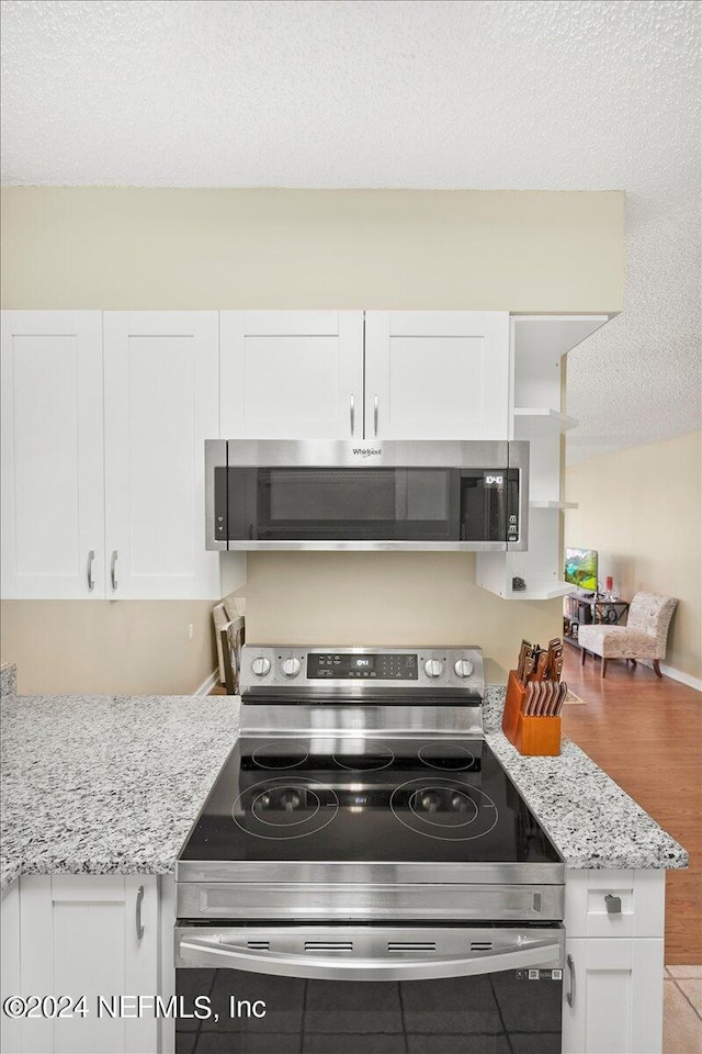 kitchen featuring appliances with stainless steel finishes, a textured ceiling, white cabinetry, and light stone counters