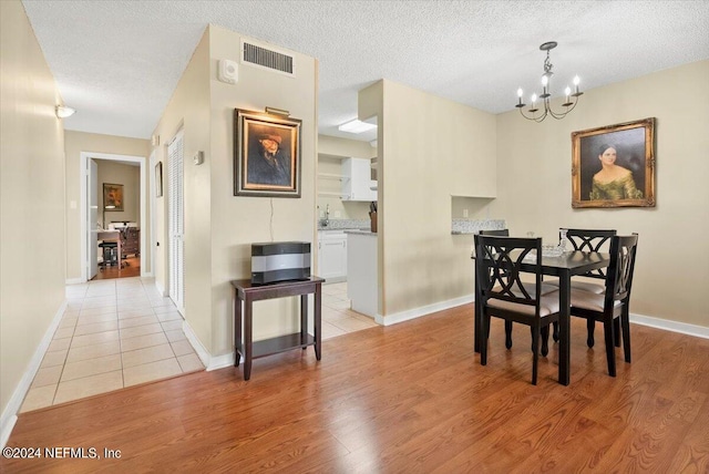 dining area featuring a textured ceiling, light hardwood / wood-style floors, and an inviting chandelier