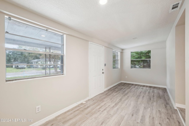 empty room with light hardwood / wood-style flooring, a textured ceiling, and plenty of natural light