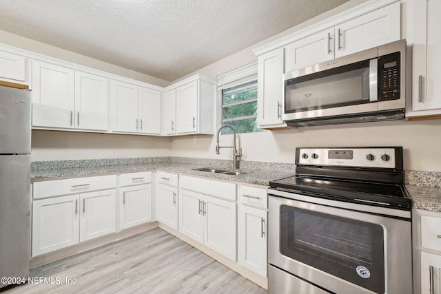 kitchen with sink, white cabinetry, light hardwood / wood-style floors, stainless steel appliances, and light stone counters