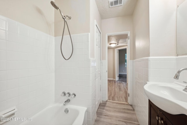 bathroom with hardwood / wood-style floors, a textured ceiling, tile walls, vanity, and shower / bath combination