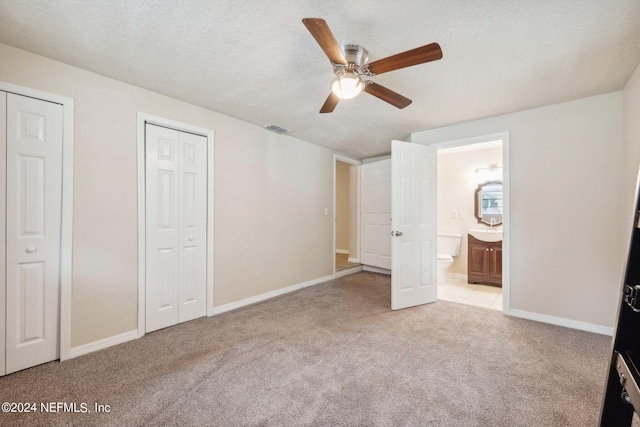 unfurnished bedroom with connected bathroom, light carpet, two closets, a textured ceiling, and ceiling fan