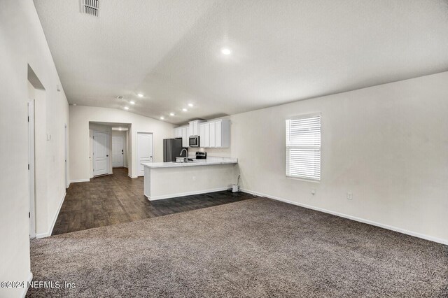 kitchen featuring dark carpet, kitchen peninsula, vaulted ceiling, white cabinetry, and stainless steel appliances