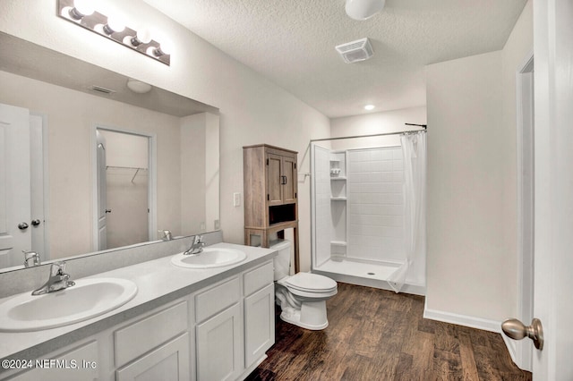 bathroom featuring walk in shower, vanity, a textured ceiling, hardwood / wood-style flooring, and toilet