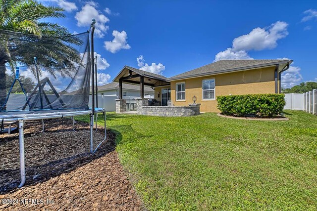 back of house featuring a trampoline, a lawn, and a patio area