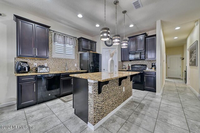 kitchen featuring black appliances, tasteful backsplash, an island with sink, and decorative light fixtures