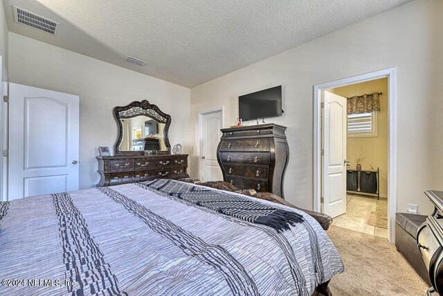 bedroom with a textured ceiling, light colored carpet, and ensuite bathroom