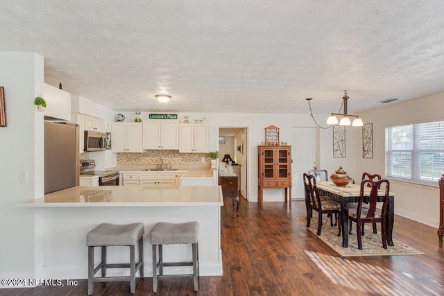 kitchen featuring dark hardwood / wood-style floors, kitchen peninsula, sink, decorative light fixtures, and appliances with stainless steel finishes