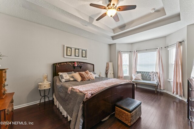 bedroom with ceiling fan, dark hardwood / wood-style flooring, a textured ceiling, and a tray ceiling