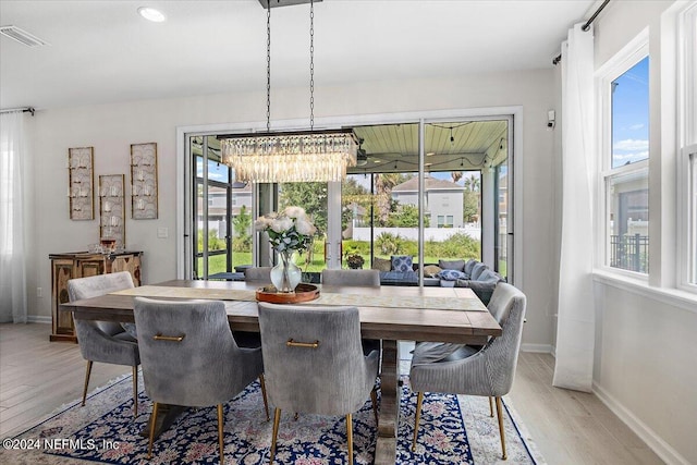 dining room featuring light wood-type flooring, a healthy amount of sunlight, and a notable chandelier