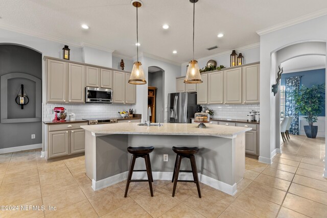 kitchen with sink, appliances with stainless steel finishes, light stone countertops, a kitchen island with sink, and backsplash