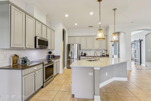 kitchen with sink, light tile patterned floors, stainless steel appliances, decorative light fixtures, and a barn door