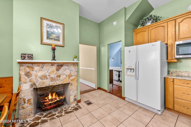 kitchen with light tile patterned flooring, white refrigerator with ice dispenser, and a fireplace