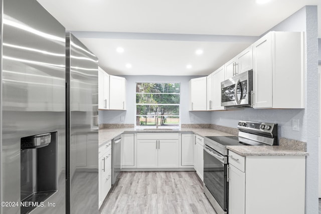 kitchen featuring light stone counters, appliances with stainless steel finishes, white cabinetry, light hardwood / wood-style floors, and sink