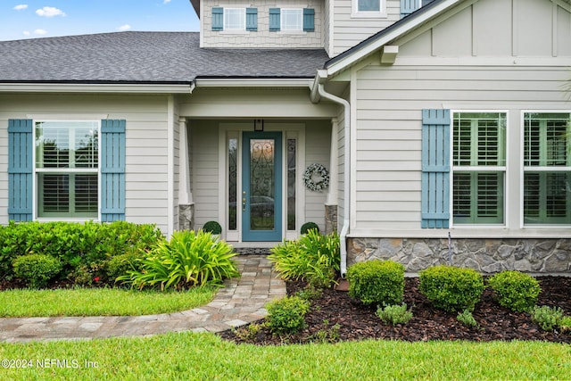 doorway to property with a shingled roof and stone siding