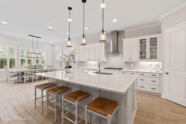 kitchen featuring sink, white cabinetry, wall chimney exhaust hood, a kitchen bar, and a spacious island