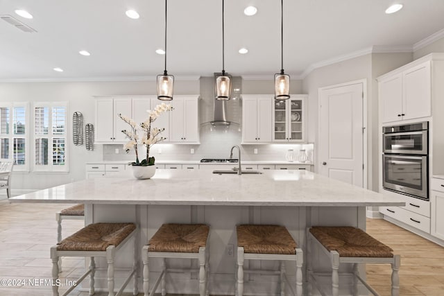 kitchen with sink, a breakfast bar area, wall chimney range hood, and an island with sink