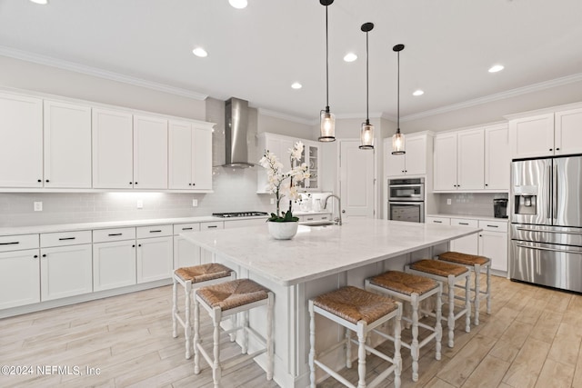 kitchen with a sink, stainless steel appliances, wall chimney exhaust hood, and white cabinetry