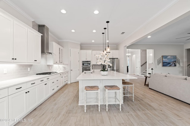 kitchen with stainless steel appliances, an island with sink, decorative backsplash, wall chimney exhaust hood, and white cabinets