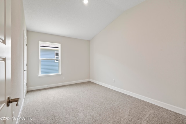 carpeted spare room with a textured ceiling and lofted ceiling