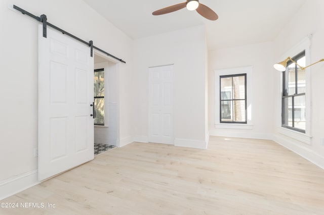 empty room featuring ceiling fan, a barn door, and light wood-type flooring